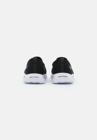 Black mesh sneakers with white soles, featuring a textured design, rear pull tab, and embossed logo on the heel.