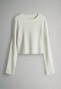 Balta, īsa garām piedurknēm augšdaļa ar ribotu tekstūru un apaļu izgriezumu. Piedurknes ir garas, un forma ir brīva. Vienkāršs un minimālistisks dizains.