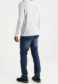 Camicia a maniche lunghe grigia in tessuto testurizzato, abbinata a jeans blu in denim con un design sbiadito e due tasche posteriori. Scarpe nere completano il look.