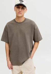 Olivo zelena ohlapna majica iz gladkega blaga, z okroglim izrezom in kratkimi rokavi. Kombinirana z bež hlačami.