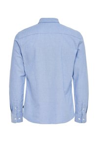 Camisa azul claro de botones con mangas largas, cuello clásico, textura suave y puños con botones. Presenta una pechera en la parte trasera.