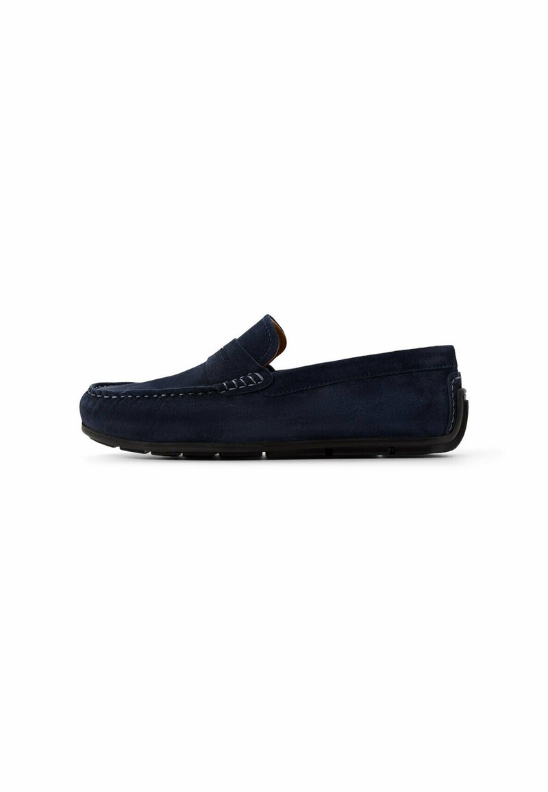 Mocassino slip-on in suede blu navy con accenti cuciti, suola piatta in gomma e punta arrotondata. Design minimale senza adornamenti aggiuntivi.