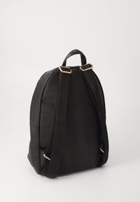 Zaino nero in tessuto, dalla forma arrotondata, dotato di due spallacci regolabili e dettagli in metallo dorato. Texture liscia con minimalismo nei dettagli.