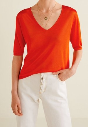 Rode korte mouwen V-hals trui gemaakt van zachte gebreide stof, gecombineerd met hoge taille witte jeans met een knoopsluiting en zakken.