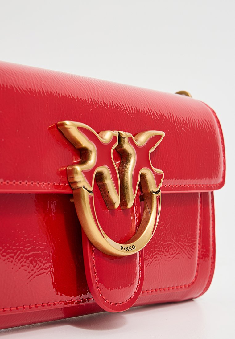Czerwona torebka z lakierowanej skóry z złotym zapięciem w kształcie motyla i wygrawerowanym napisem "PINKO" na zapięciu pierścienia.