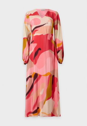 Femme portant une longue robe fluide avec des motifs abstraits rose, rouge, orange et beige, associée à des chaussures plates noires.