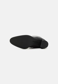 Zapato de cuero negro con punta lisa, tacón bajo y suela de goma texturizada. Presenta un sutil logo en el talón y un diseño aerodinámico.