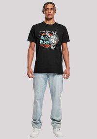 Svart bomull T-skjorte med et fargerikt Bugs Bunny-trykk og teksten "Vintage Collections," kombinert med lyseblå jeans og hvite joggesko.