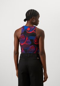 Večbarvna majica brez rokavov z rožnim potiskom v odtenkih rdeče in modre, združena s črnimi hlačami z visokim pasom. Gladek teksturo, oprijet dizajn.