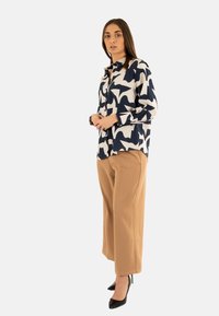 Blusa de rayas en azul marino y crema con mangas largas, cierre de botones en la parte delantera, combinada con pantalones de pierna ancha en color tostado y tacones altos negros.