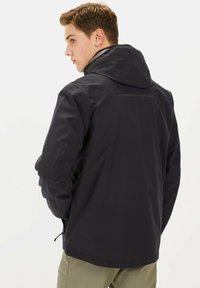 Zwarte hoodie met een textuur, ritszakken en een reflecterende strip op de rug. Lichtgewicht, ontworpen voor buitengebruik.
