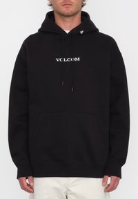 Hoodie noir avec le logo "VOLCOM" blanc sur la poitrine, capuche avec cordon de serrage et poche frontale. Présente des poignets et un ourlet côtelés pour un ajustement confortable.