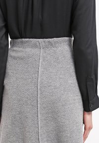 Jupe grise à carreaux houndstooth avec une finition texturée, dotée d'une taille ajustée, associée à un blouse noire à manches longues.