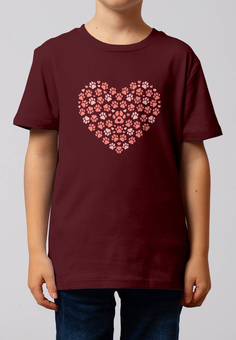 Enfant portant un t-shirt bordeaux avec un cœur formé de diverses empreintes de pattes roses et rouges de différentes tailles à l'avant.