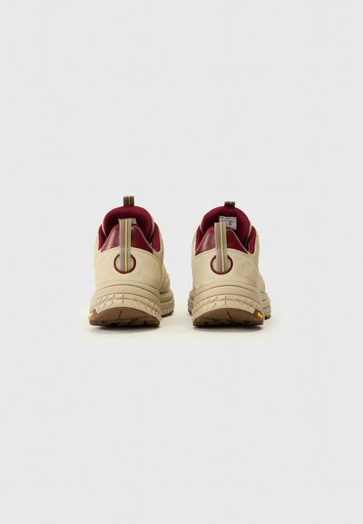 Bottes de sport beige avec un dessus texturé, des accents rouges et une languette. Caractéristiques d'une semelle robuste avec un motif pour une meilleure adhérence.