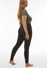 Musta legginsit, joissa on istuva muotoilu, korkea vyötärönauha ja takataskut. Malli käyttää vihreää ribbineulottua lyhythihaista toppia.