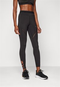 Černé sportovní legíny s síťovými výřezy a křížovým detailem na kotnících, vyrobené z hladké a pružné látky s vysokým pasem.