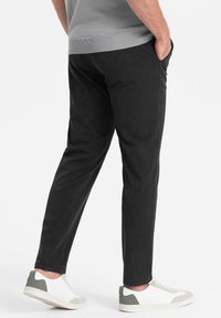 Donkergrijze taps toelopende broek met een gladde textuur en zijzakken, gecombineerd met witte en grijze sneakers. Eenvoudig, minimalistisch ontwerp.