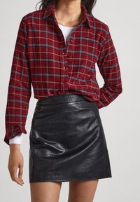 Ruitjeshemd in rood en blauw met knoopsluiting en lange mouwen, gecombineerd met een zwarte leren minirok, benadrukt door een gestructureerde zwarte riem.