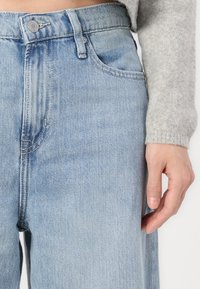 Svetlo modre denim hlače z visokim pasom, z gumbom za zapiranje, klasičnim petimi žepi in subtilnimi detajli whisker.