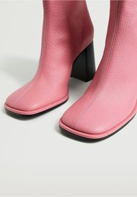 Paire de bottines en cuir rose avec bouts carrés et talons carrés hauts sur une surface gris clair.