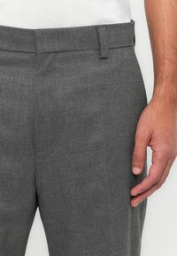 Gray tailored trousers with a smooth texture, featuring a flat front, belt loops, and a side pocket, paired with a white shirt.