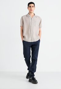 Light beige short-sleeve shirt with buttons and pocket; paired with dark navy trousers and black platform shoes; minimalistic design.