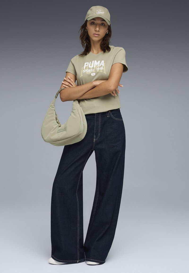 Lys olivengrøn cropped t-shirt med "PUMA" print, parret med mørkeblå løse jeans og en blød taske i matchende grøn, båret med en kasket.