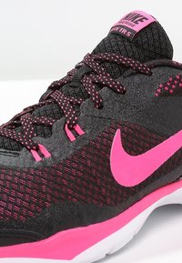 Sort træningssko med pink detaljer; mesh-overdel, tekstureret overflade, kraftigt pink Nike-logo og kontrastfuld hvid sål. Designet til træningsformål.