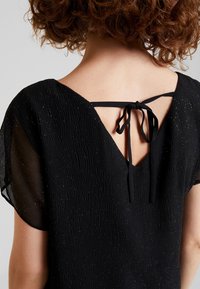 Black dress with textured fabric featuring a subtle shimmer, wide short sleeves, and a V-shaped back tied with black ribbons.