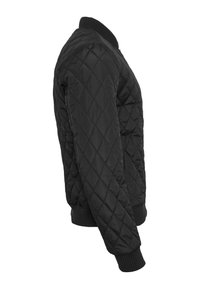 Veste matelassée noire avec surpiqûres en losange, col, poignets et ceinture côtelés, vue de côté droit.