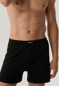 Czarne bokserki wykonane z gładkiego materiału z elastycznym pasem. Posiadają dwa guziki z przodu oraz nazwę marki "ATLANTIC" na pasie.
