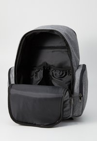 Γκρι υφασμάτινος σακίδιο με ευρύχωρο εσωτερικό, που διαθέτει φερμουάρ και ελαστικές τσέπες. Η μπροστινή πλευρά έχει μια μαύρη θήκη με φερμουάρ.