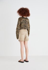 Jersey de leopardo con mangas sueltas, combinado con pantalones cortos de pana color beige. Sandalias negras tipo slip-on. Fondo neutro.
