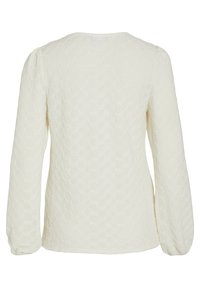 Haut crème texturé à manches longues avec un motif de nid d'abeille, présentant un col rond et des manches froncées. Dos uni sans embellissements.