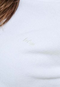 Pull en tricot blanc avec un tissu texturé, col rond et logo brodé subtil dans un fil assorti. Confortable, légèrement décontracté.