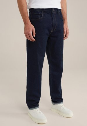 Donkerblauwe denim jeans hebben een rechte pijp, een standaard vijf-pocket ontwerp en contrasterende stiksels. Gecombineerd met witte sneakers.