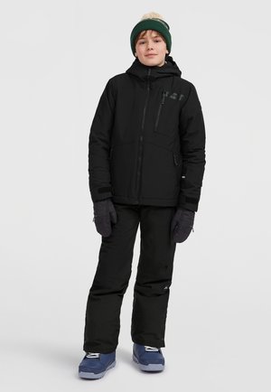 Černá sněhová bunda s kapucí, zipovými kapsami a fialovými rukavicemi. Černé sněhové kalhoty a modré boty s bílými tkaničkami dokončují outfit.