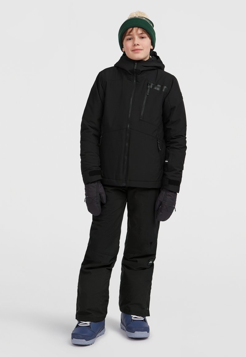 Zwarte sneeuwjas met een capuchon, ritszakken en paarse handschoenen. Zwarte sneeuwbroeken en blauwe laarzen met witte veters maken de outfit compleet.