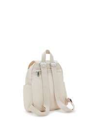 Mochila de tela beige con dos correas ajustables, asa superior, cierre de cremallera y herrajes plateados. Presenta bolsillos laterales para almacenamiento.