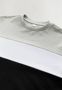 Grå, hvid og sort stribet t-shirt med rund halsudskæring, der har ribbet tekstur, korte ærmer og et mærke ved halsudskæringen.