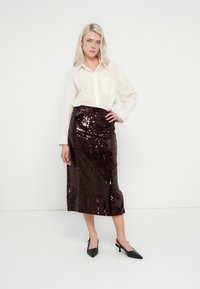 Jupe midi à sequins en bordeaux profond avec une taille froncée. Associée à une chemise blanche boutonnée et des escarpins noirs à bout pointu.