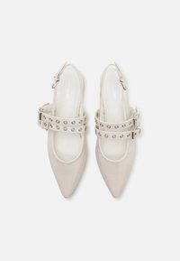 Chaussures slingback en cuir verni beige avec des pointes aiguisées, des brides à double boucle avec des accents métalliques et une texture lisse.