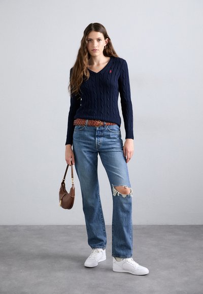 Navy cable-knit sweater with V-neck, paired with light blue distressed jeans and white sneakers. Accented with a braided brown belt and handbag.