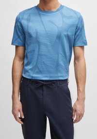 Blå kortärmad t-shirt med en strukturerad yta och ett abstrakt mönster, tillsammans med marinblå byxor med dragsko i midjan.