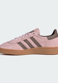 Sapatilhas de camurça rosa com três riscas castanhas, sola de borracha gum e bico arredondado. Apresentam atacadores e um colar acolchoado para conforto.