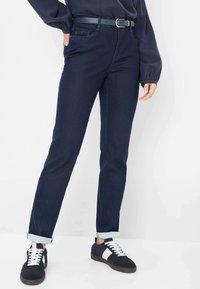 Jeans in denim blu scuro con vestibilità dritta, caratterizzati da orli arrotolati, tasche frontali e una cintura nera con una fibbia rettangolare.