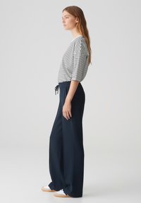 Gestreepte, losse top met driekwart mouwen, gecombineerd met hoge, donkerblauwe wijde broek en witte sneakers.