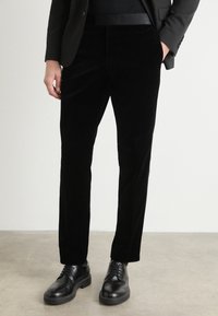Fekete bársony nadrág slim fit szabásban, lapos el�ülső résszel és oldalsó zsebekkel, csillogó fekete fűzős cipővel párosítva.