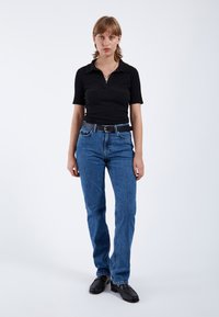 Polo negro de canalé con mangas cortas, combinado con jeans de pierna recta azules y zapatos negros. Los accesorios incluyen un collar de plata.